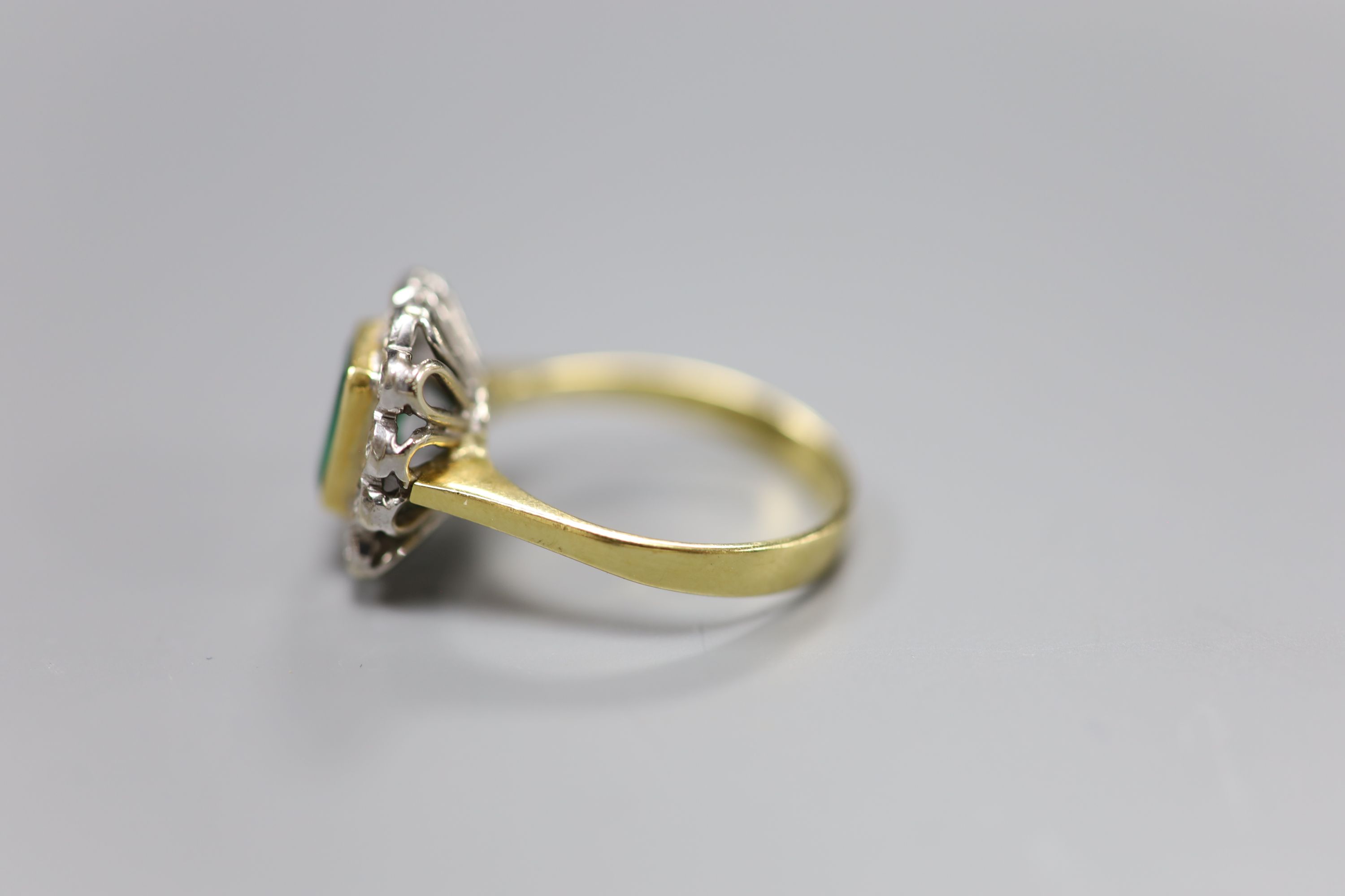 An emerald and diamond cluster ring, white and yellow metal setting (tests as 18ct), size Q, gross 6g.